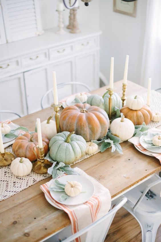 An all natural Thanksgiving centerpiece of lots of fresh pumpkins stacked and some tall and thin candles in gilded candleholders