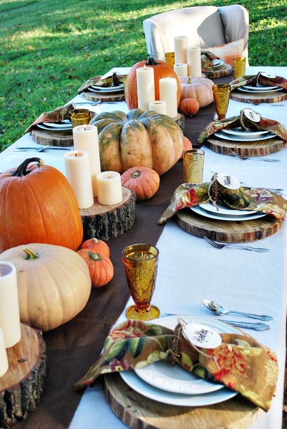 an all-natural Thanksgiving tablescape with tree stumps, heirloom pumpkins, candles, bright printed napkins and colored glasses