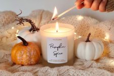 an easy fall or Thanksgiving decoration of a neutral knit blanket, some faux pumpkins, lights and a candle in a jar