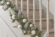 an evergreen garland with silver and matte silver ornaments and bottle brush Christmas trees is a chic idea for styling a staircase
