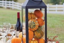 an oversized lantern filled with pumpkins and with berries is a cool rustic decoration you can easily make