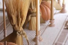 bundles of wheat and tall and thin natural-colored candles in wooden candleholders plus natural-colored pumpkins and a striped runner