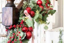 chic Christmas banister decor with evergreens and foliage, red ornaments, berries and a red and white striped ribbon is cool