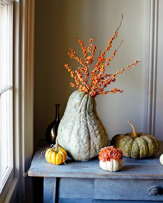 Heirloom pumpkins with blooms and an oversized gourd with berried branches is a lovely all natural decoration