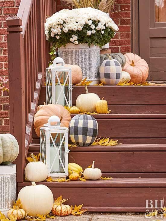 neutral and plaid pumpkins, bright leaves, candle lanterns and white blooms in a pot for decorating outdoors