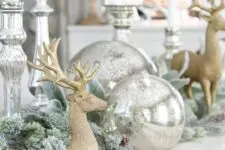 vintage Christmas decor with large silver ornaments, silver candleholders, snowy evergreens and gold deer