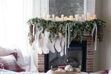 a Christmas mantel with an evergreen and light garland, pillar candles, striped ribbons and white stockings is a gorgeous idea