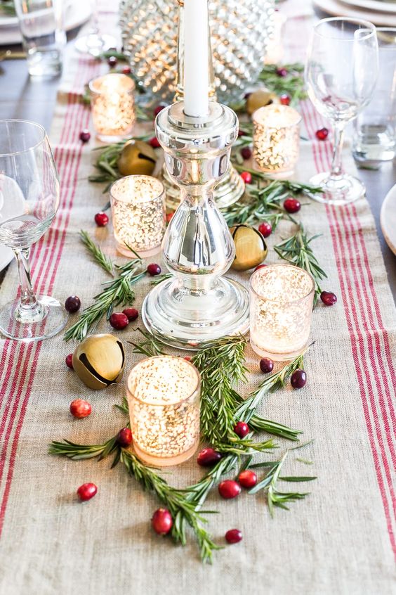 a beautiful Christmas centerpiece with greenery, berries, mercury glass candleholders, large bells and a striped runner