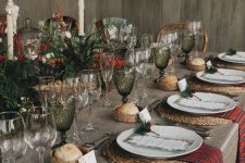 a beautiful Christmas tablescape with evergreens, berries, tall candles, green glasses, woven placemats, red napkins and printed menus