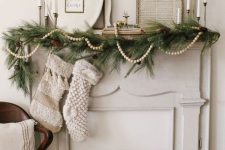 a beautiful vintage Christmas mantel with an evergreen and pinecone garland, a pompom one, vintage frame pictures and candles