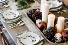 a bold farmhouse Christmas tablescape with evergreens, a wooden bowl with pinecones, pomegranates and pillar candles, neutral linens