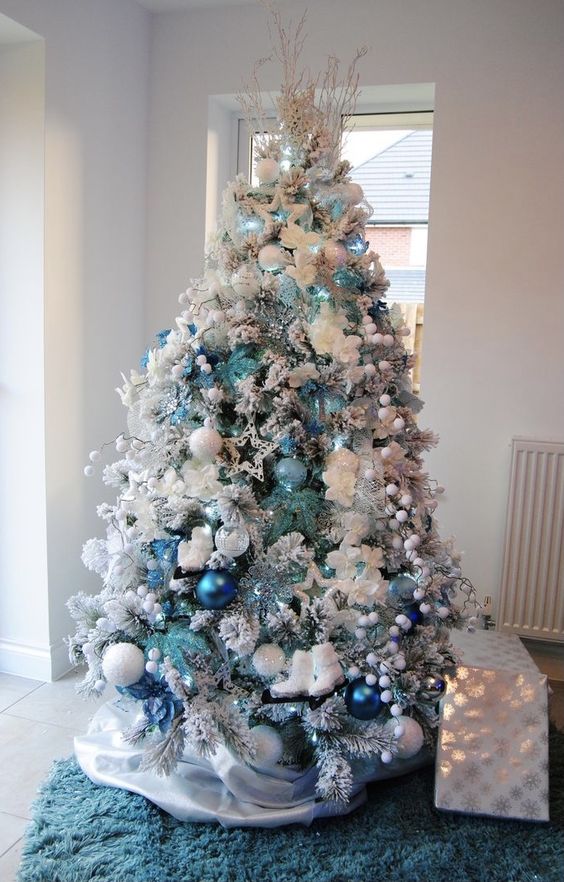 A classic flocked Christmas tree with light blue, navy, white snowball inspired ornaments, lights, pompoms and stars is wow