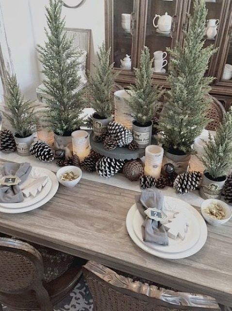 a classy Christmas tablescape with usual and snowy pinecones, potted Christmas trees, neutral linens and Christmas trees on place settings
