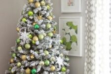 a flocked Christmas tree with neon green, emerald and gold ornaments, snowflakes and a star topper is a cool idea