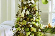 a green Christmas tree with white and green blooms and ornaments, branches, ribbons and pinecones is a chic idea