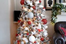 a lovely modern flocked Christmas tree with oversized white, silver and red textural ornaments, smaller ones, plaid ribbons and faux snow plus lights