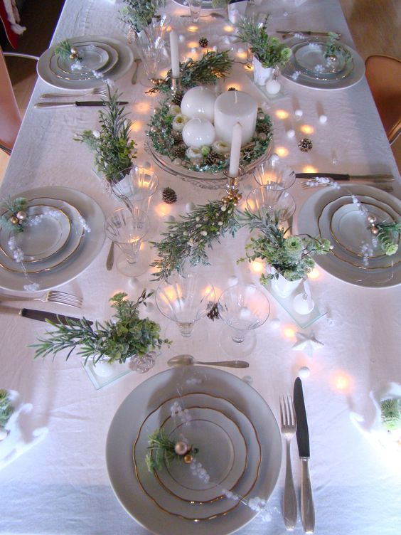 a neutral shiny Christmas tablescape with a centerpiece of candles and greenery, lights, flocked branches, mini ornaments and tall and thin candles