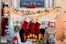 a ski lodge Christmas mantel with a snowy evergreen garland with red berries, a pompom garland, red stockings and mismatching signs