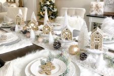 a super cute Christmas tablescape with a white faux snow table runner and faux fur placemats, snowy pinecones, gold ornaments, white bottle brush trees and gingerbread houses
