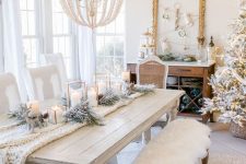 a white Christmas tablescape with a knit table runner, flocked greenery, candle lanterns and deer and a beaded chandelier over the table