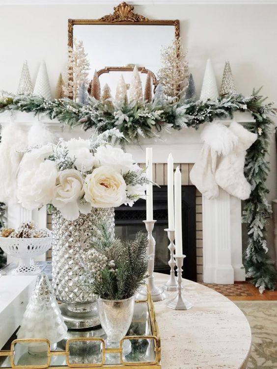 a winter wonderland mantel with a snowy evergreen garland, faux fur stockings, mini Christmas trees and a mirror in a chic frame