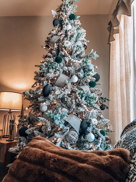 an elegant flocked Christmas tree decorated with white, black and dark green ornaments, leaves, ribbons and wooden beads