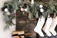 an elegant modern Christmas mantel with an evergreen, white, silver, copper ornament and pinecone garland and white stockings