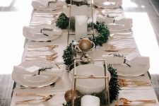 an elegant neutral Christmas tablescape with white linens, gold cutlery, gold and gold glitter ornaments, a greenery garland and pillar candles