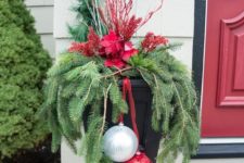 an outdoor urn with evergreens, white branches, red blooms and a giant silver and red ornament