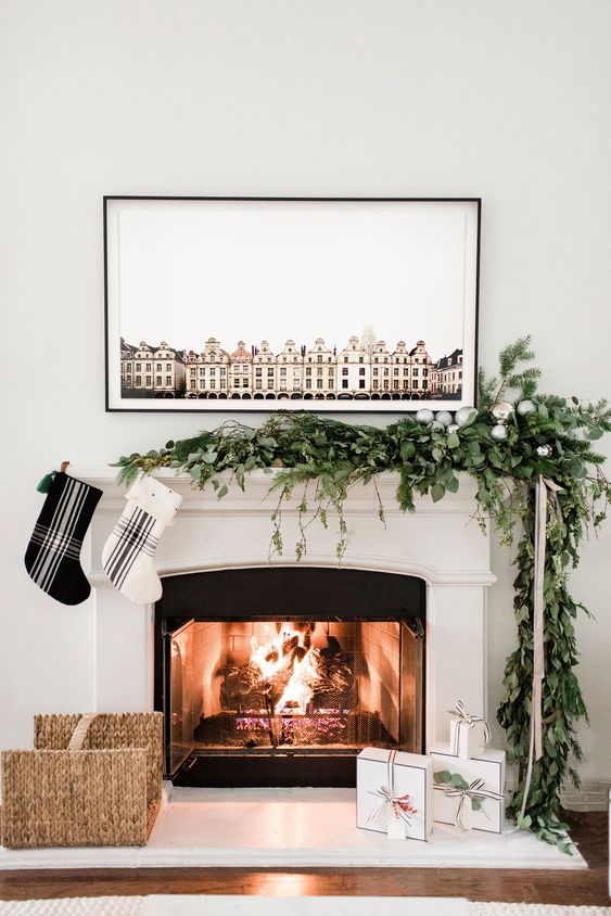 an ultra-modern Christmas mantel with a greenery and evergreen garland with silver ornaments, and a duo of black and white plaid stockings