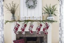 plaid stockings, an evergreen garland with wooden beads, candles in gilded candle holders and a snowy wreath over the mantel for a traditional Christmas look