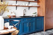 a bold blue kitchen with a printed tile floor, wooden shelves and a storage unit, black chairs with cushions is welcoming
