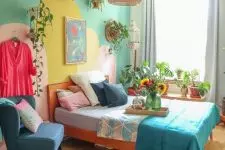 a bright bedroom for a teenager, with a green and yellow accent wall, a stained bed with colorful bedding, a blue chair, potted greenery