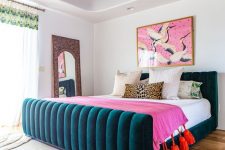 a bright bedroom with a floral ceiling, a teal upholstered bed, bright bedding, a colorful artwork and a mirror in a carved frame