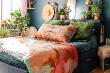 a bright bedroom with navy walls and a black storage bed, colorful bedding, potted plants, a mirror and brass lamps is a fun and bold space