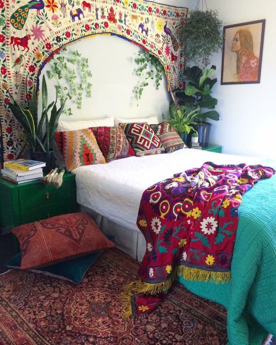 a bright boho bedroom with a bed with bright bedding and pillows, a rug, emerald nightstands, a colorful artwork over the bed