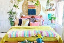 a bright boho bedroom with colorful bedding and pillows, a bold artwork and colorful macrame plus bright pots