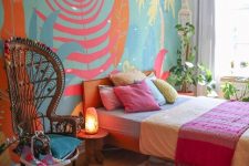 a bright boho sleeping space with a wall mural, a bed with colorful bedding and a rug, a woven pendant lamp and a papasan chair