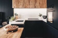 a chic black kitchen with a wooden table and a large hood plus white countertops looks very stylish and bold