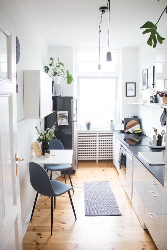 a chic white kitchen with black countertops, open shelves, a folding table and grey chairs plus plants