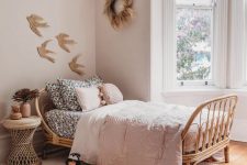 a dreamy boho girl’s room with light pink walls, a rattan bed with blush and black and white bedding, layered rugs and a rattan nightstand
