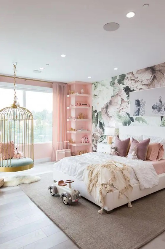 A fantastic girl's bedroom with a floral accent wall, a pink wall with built in shelves, a white bed with pink bedding, a cage pendant chair