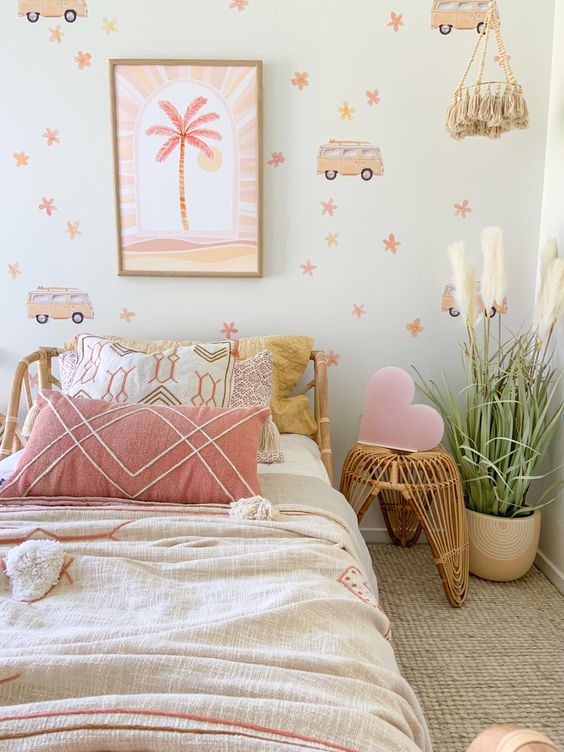 a fun girl's room with printed wallpaper, a rattan bed with pastel bedding, a rattan nightstand with a pink heart, a potted plant and tassels