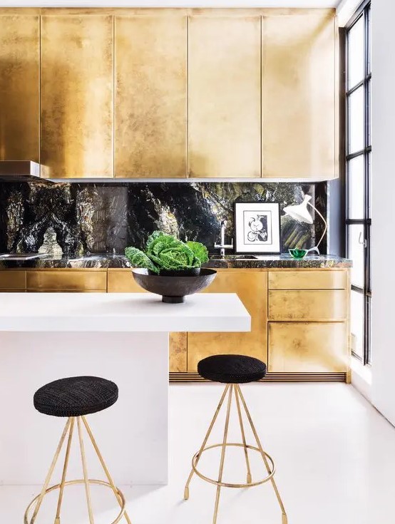 A gold kitchen with a black stone backsplash and a countertop plus a white minimalist kitchen island for a jaw dropping look