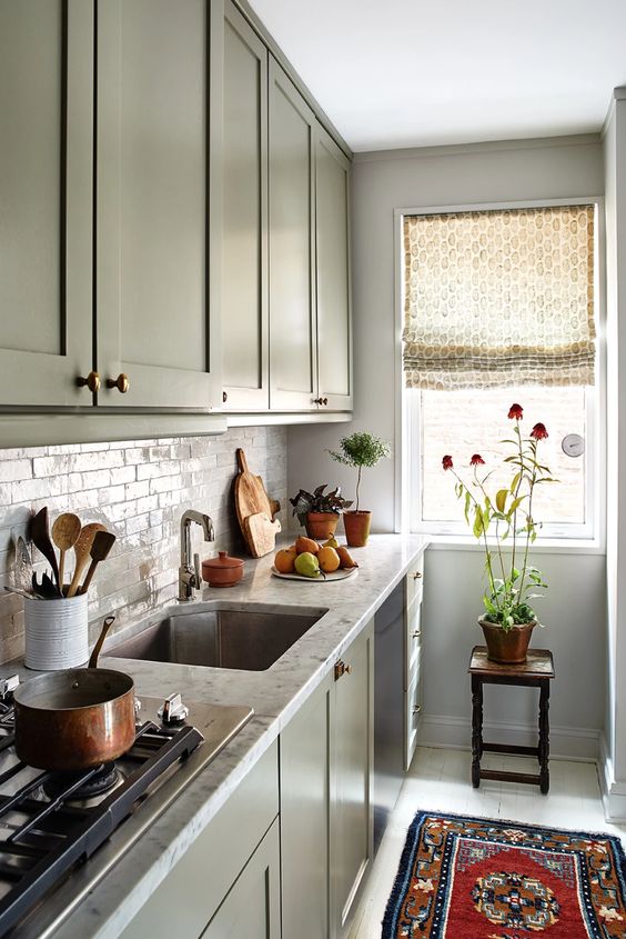 a green one wall kitchen with stone countertops and a tile backsplash and some printed textiles is chic