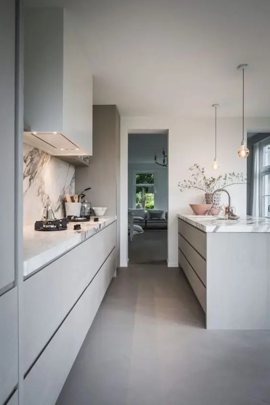 a heavenly grey contemporary kitchen with sleek cabinets and a large kitchen island, a white stone backsplash and countertops and pendant lamps