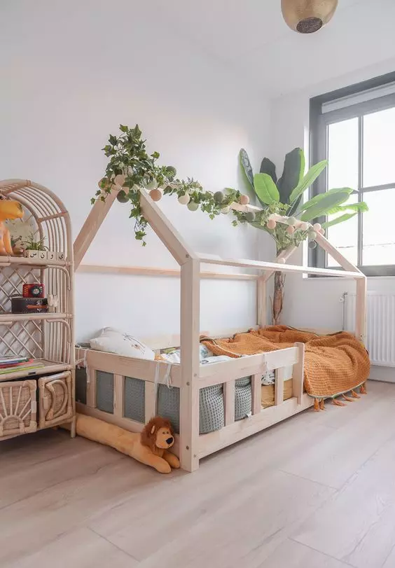 a jungle-themed kid's room with a house-shaped bed, greenery, a rattan storage unit, some green and mustard bedding