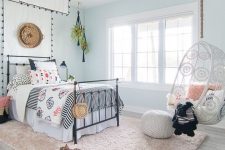 a lovely coastal girl bedroom with light blue walls, a black metal bed with a canopy, a pendant chair and a fluffy rug