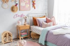 a lovely girl’s room with a metal bed with pastel bedding and layered rugs, a rattan nightstand and a storage unit, a gallery wall