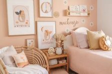 a lovely girl’s room with a peachy accent wall and peachy bedding, stained and wicker furniture, a gallery wall and pillows